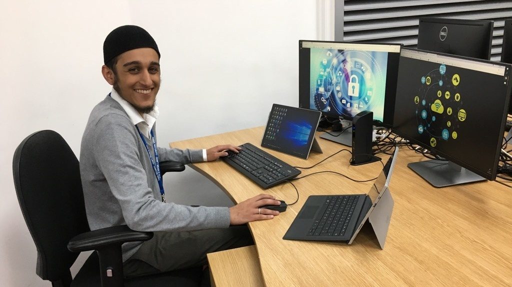 Ismail Ghafoor sitting at a desk with 2 laptops and several large screens
